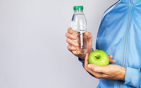 Young Sporty Man holding Green Apple and Bottle of Water. Sport or Healthy Life Concept. Horizontal with Copy Space