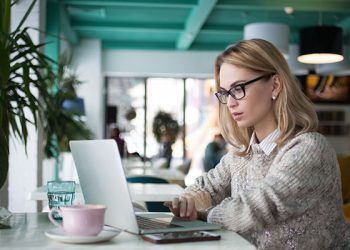 Concentrated female student preparing for exam in cafe. Busy young businesswoman using laptop to work. She reading business article. Lifestyle concept