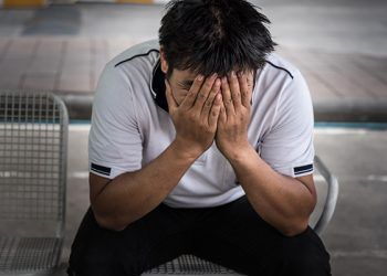 Man fired from job sitting hold the head with hand and worried stressed face expression outside office