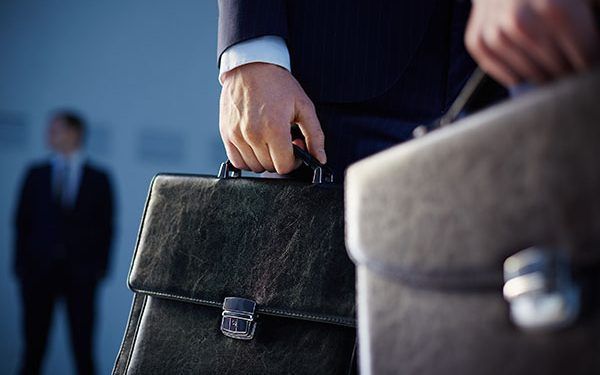 Cropped image of business partners carrying briefcases on the foreground while their colleague standing on the background