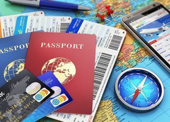 Creative abstract business travel and tourism concept: air tickets or boarding pass, passports, touchscreen smartphone with online airline tickets booking or reservation internet application, magnetic compass, credit cards and pen on world geographic map atlas with selective focus effect