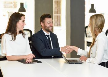 Smiling young couple shaking hands with an insurance agent or investment adviser. Three people meeting in an office reaching an agreement