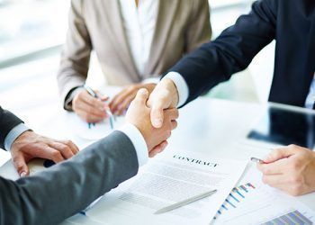 Image of business partners handshaking over business objects on workplace