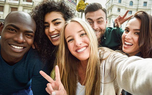 Multiracial group of friends taking selfie in a urban street with a blonde woman in foreground. Three young women and two men wearing casual clothes.