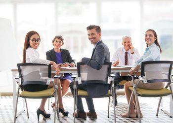 Multi-ethnic smiling business team sitting at table and looking at camera. Business executives having meeting in office. Teamwork concept