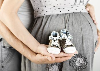 Newborn baby booties in parents hands. Pregnant woman belly.