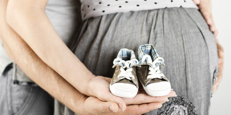 Newborn baby booties in parents hands. Pregnant woman belly.