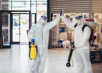 Professional workers in hazmat suits disinfecting indoor of mall, pandemic health risk, coronavirus