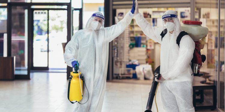 Professional workers in hazmat suits disinfecting indoor of mall, pandemic health risk, coronavirus