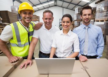 Warehouse managers and worker smiling at camera in a large warehouse