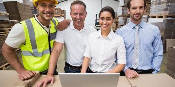 Warehouse managers and worker smiling at camera in a large warehouse