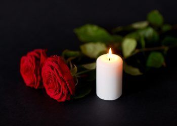 funeral and mourning concept - red roses and burning candle over black background
