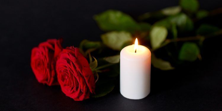 funeral and mourning concept - red roses and burning candle over black background