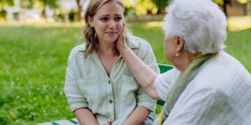 A worried senior grandmother comforting grown up granddaughter when sitting on bench in park, share problem with someone close concept