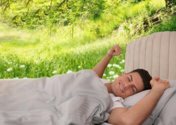 Happy man stretching in bed and beautiful view of park on background. Sleep well - stay healthy
