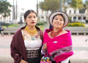 Two women showcasing vibrant indigenous fashion, adorned in traditional attire with colorful textiles and intricate jewelry, reflecting cultural pride and heritage in a lively urban setting