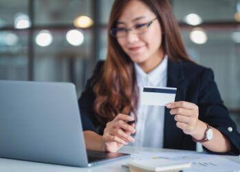 An asian businesswoman holding credit cards while using laptop computer in office