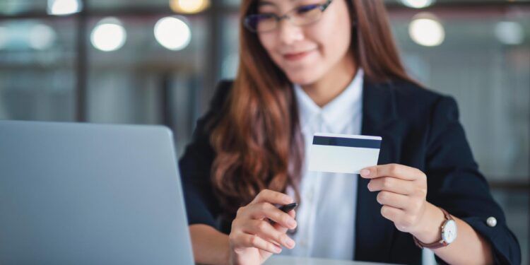 An asian businesswoman holding credit cards while using laptop computer in office